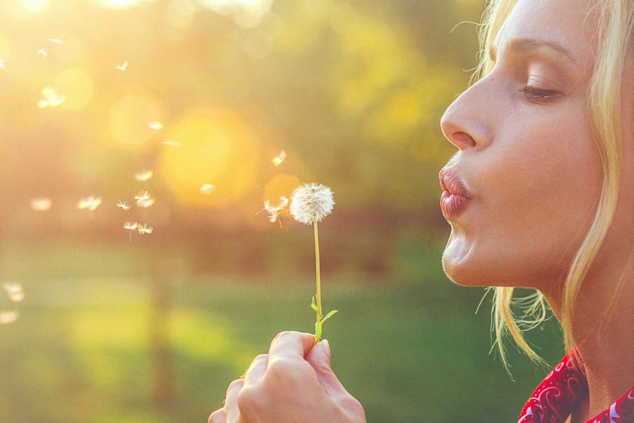 Close-up of a happy young blonde woman blowing dandelion